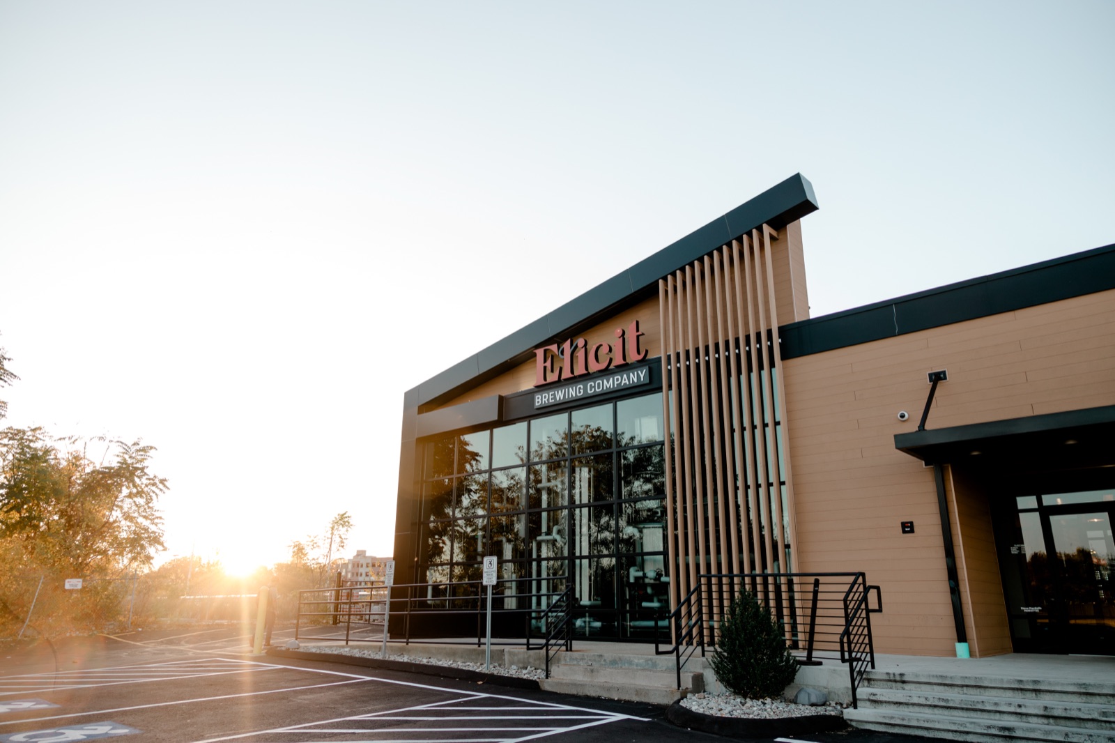 The front of Elicit Brewing Company in Fairfield, Connecticut, at sunset, with its name in red letters over a tall glass entrance.