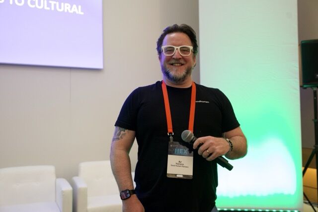 AJ Keirans on stage with a microphone and conference lanyard.