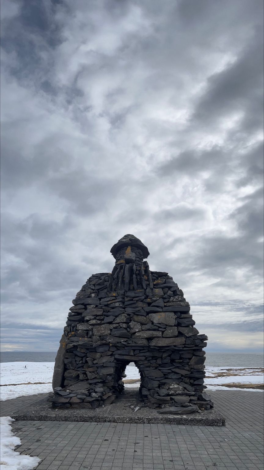 A stone sculpture of a figure with an arched opening, under a cloudy sky.