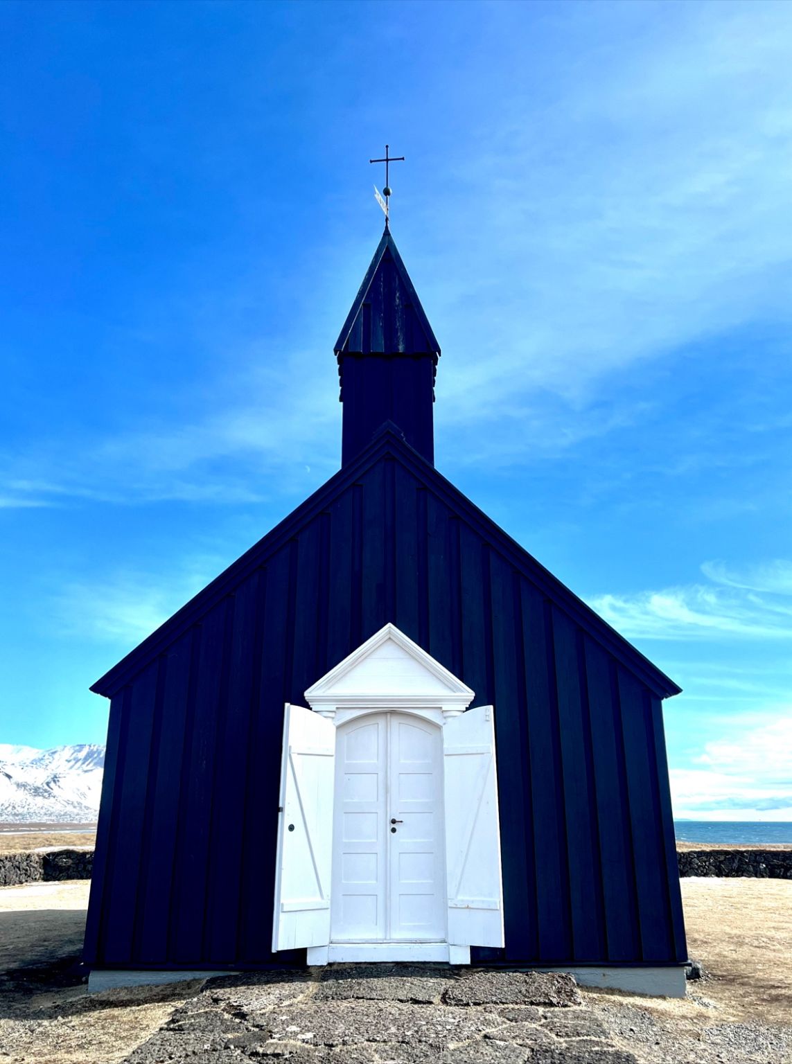 A black wooden church with a white door, seen straight on against a blue sky.
