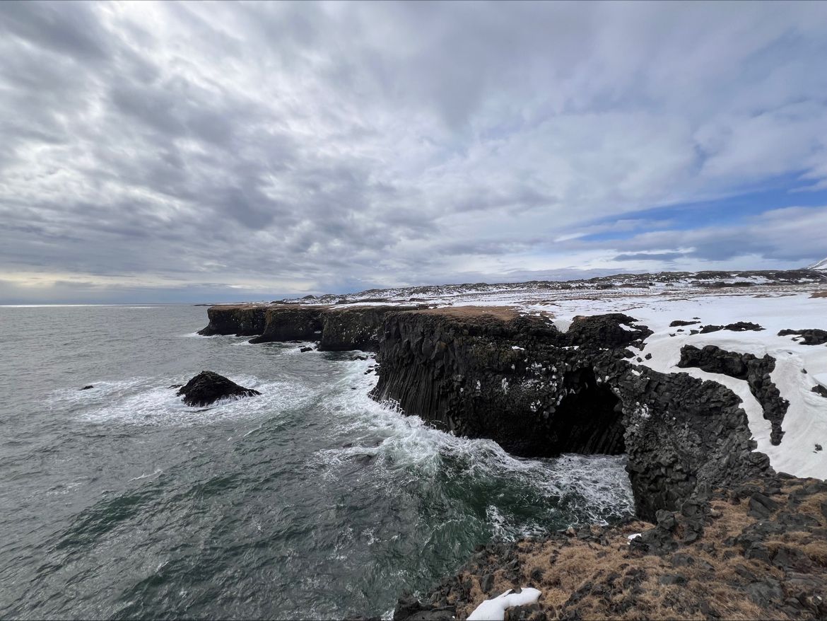 Dark sea cliffs and crashing waves along a snowy coastline.
