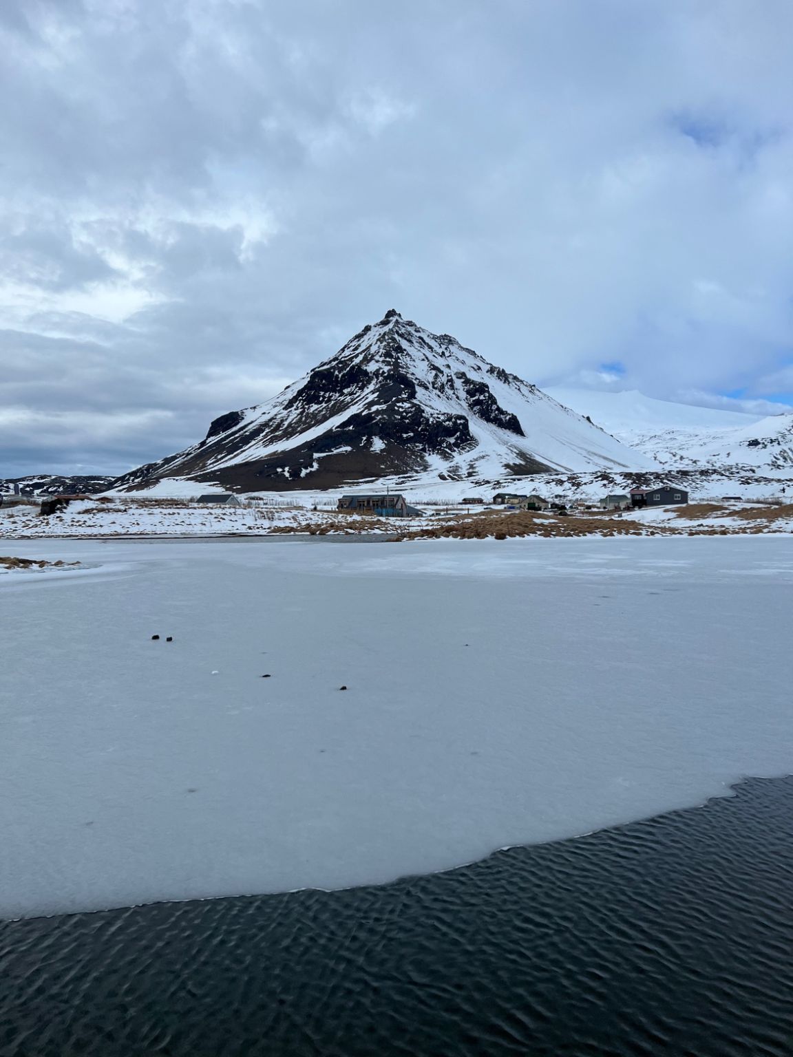 A snow-capped mountain behind a half-frozen lake.