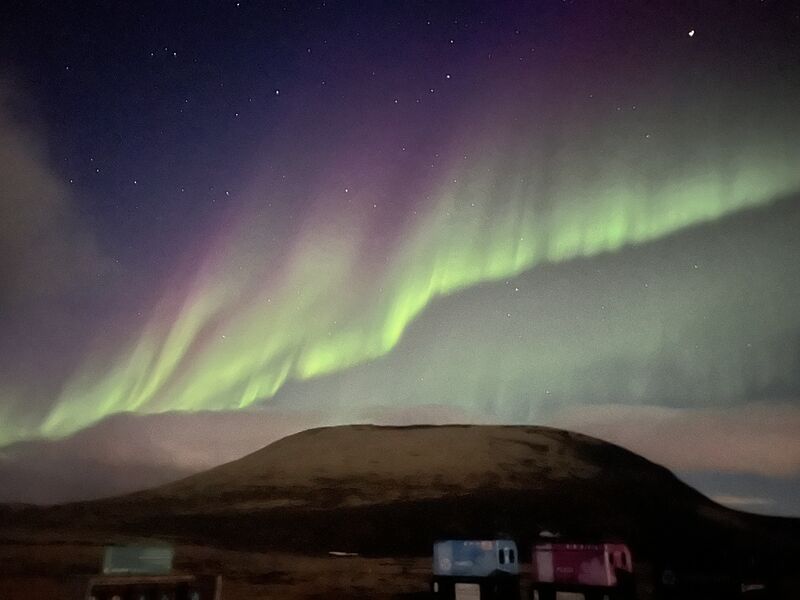 Green northern lights over a dark hill at night.