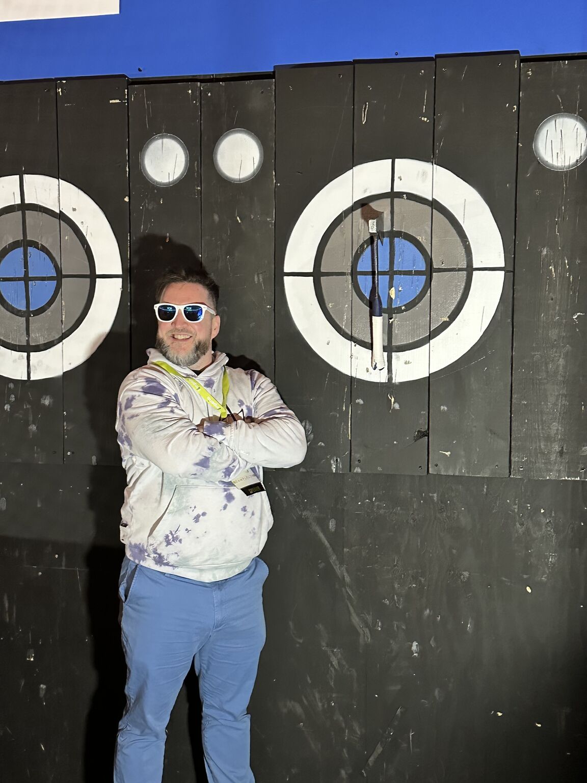 AJ Keirans in sunglasses and a tie-dye jacket in front of axe-throwing targets.