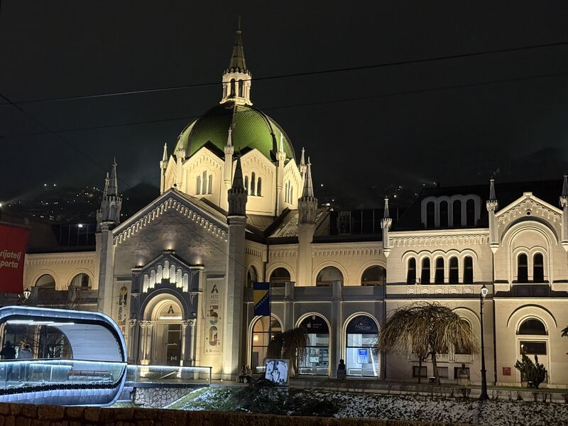 A domed historic building in Sarajevo lit up at night.